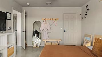 Un dormitorio con cama, televisor, armario, espejo y puerta.