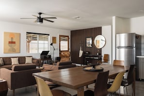 A modern living space with a dining area, sofa set, and a kitchen with a built-in refrigerator. - Dark Star - Endless Stars, Cowboy Pool, Spa, Fire pit, BBQ (Twentynine Palms)