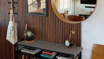 Una habitación con pared de listones de madera, un espejo redondo, un escritorio con libros, una silla de madera y un televisor.