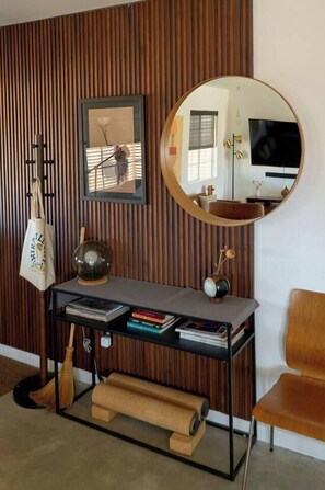 A room with a wooden slat wall, a round mirror, a desk with books, a wooden chair, and a TV. - Dark Star - Endless Stars, Cowboy Pool, Spa, Fire pit, BBQ (Twentynine Palms)