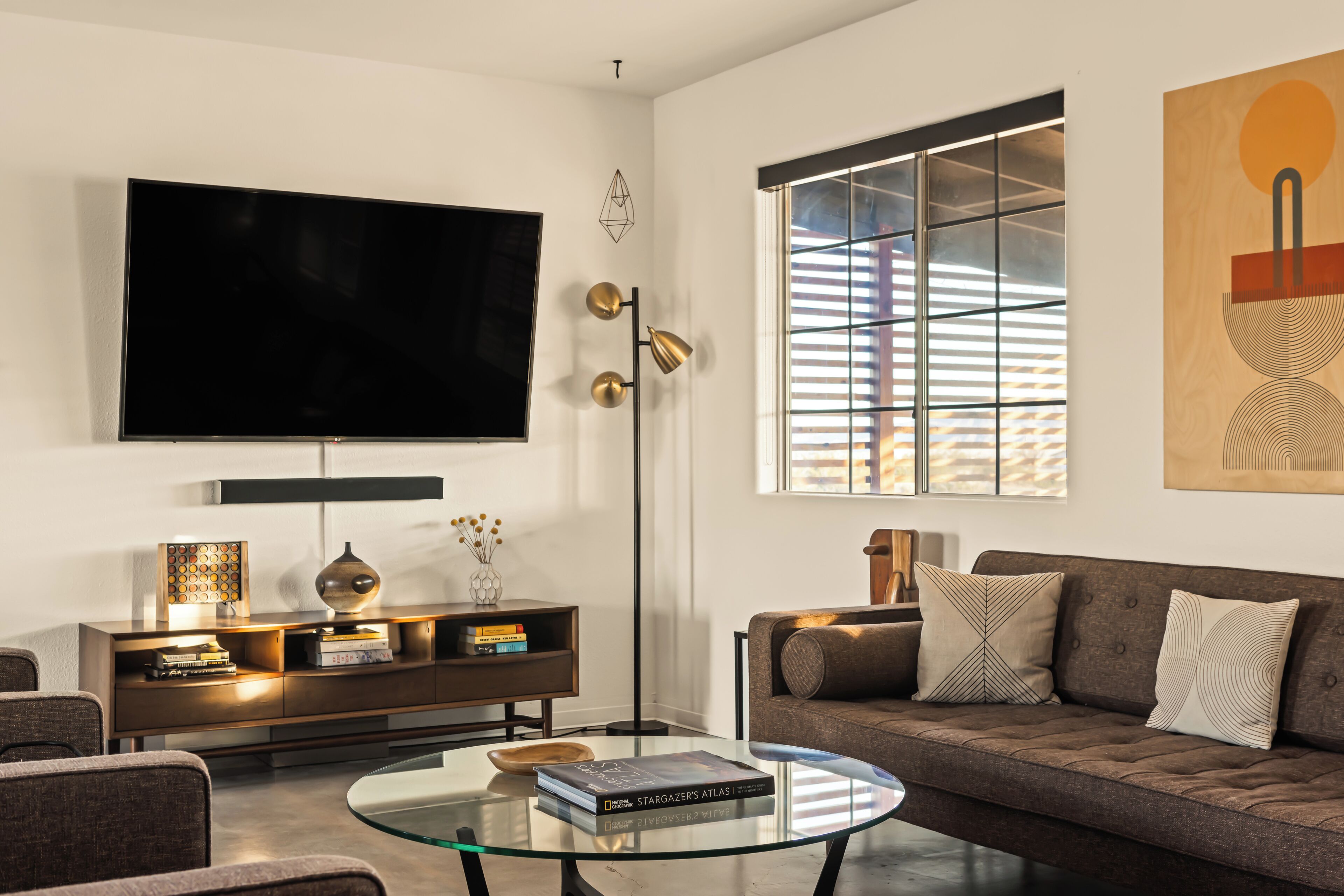 A modern living room with a large flat-screen TV, a glass coffee table, a sofa, and a bookshelf.