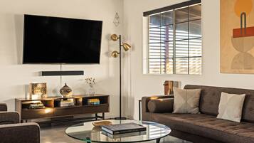 A modern living room with a large flat-screen TV, a glass coffee table, a sofa, and a bookshelf.