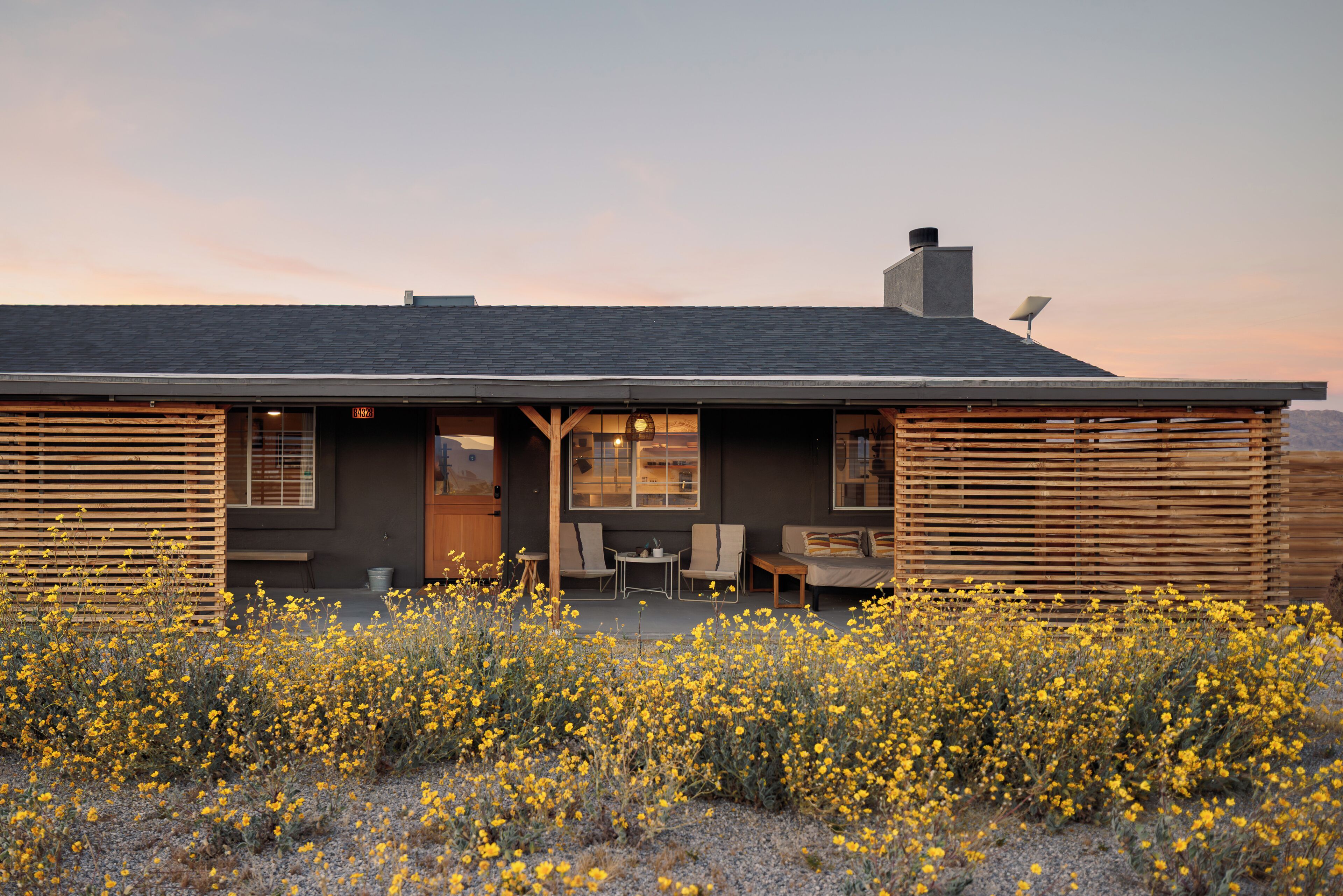 A modern house with a flat roof, large windows, and a patio area with outdoor furniture.