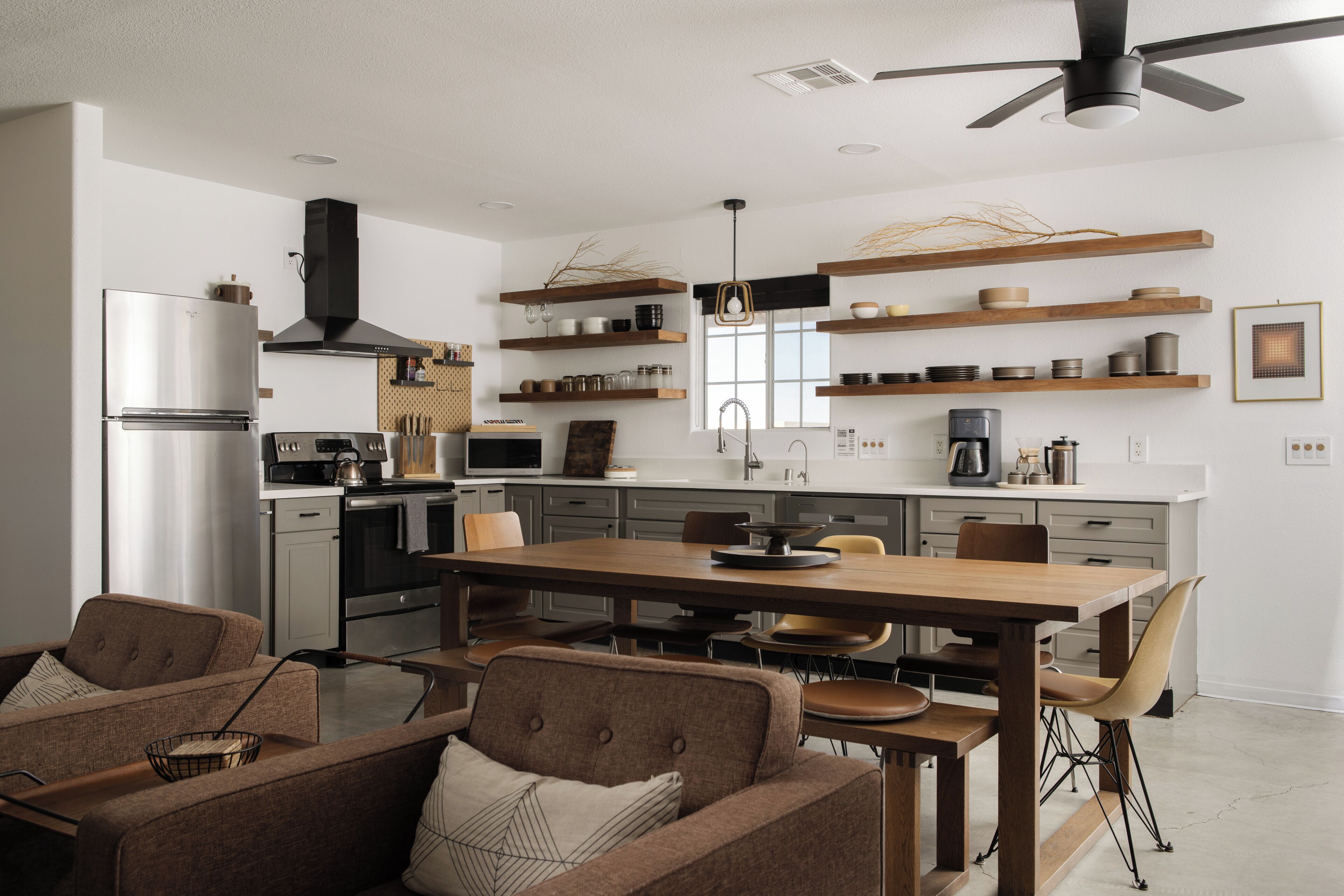 A modern kitchen with a central island, built-in appliances, and wooden shelves.