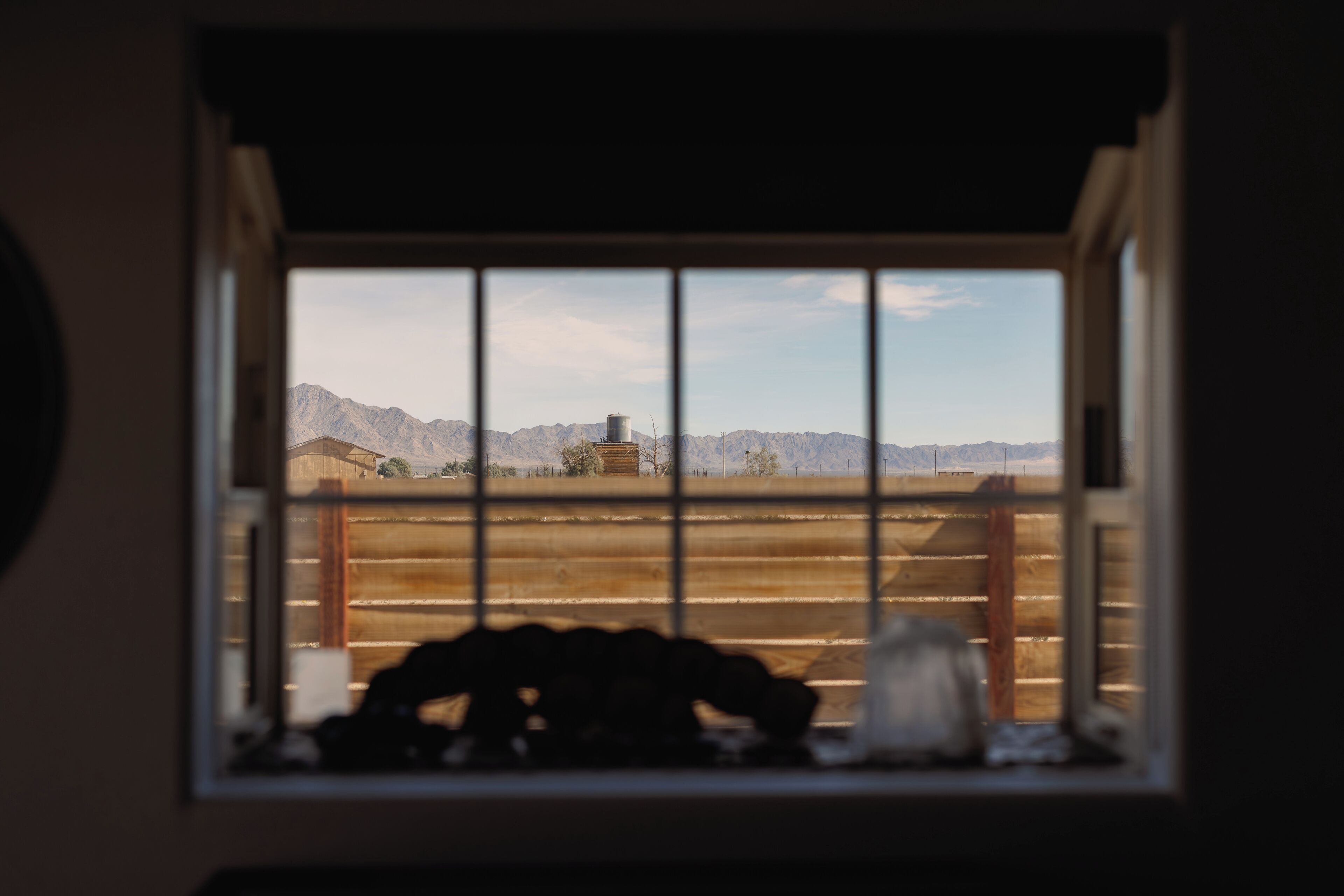 A window with a view of a mountainous landscape, a wooden fence, and a small building.