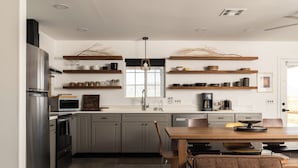 A modern kitchen with grey cabinets, stainless steel appliances, and wooden shelves.