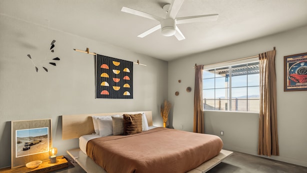 A modern bedroom with a bed, a ceiling fan, a window with curtains, and wall art.