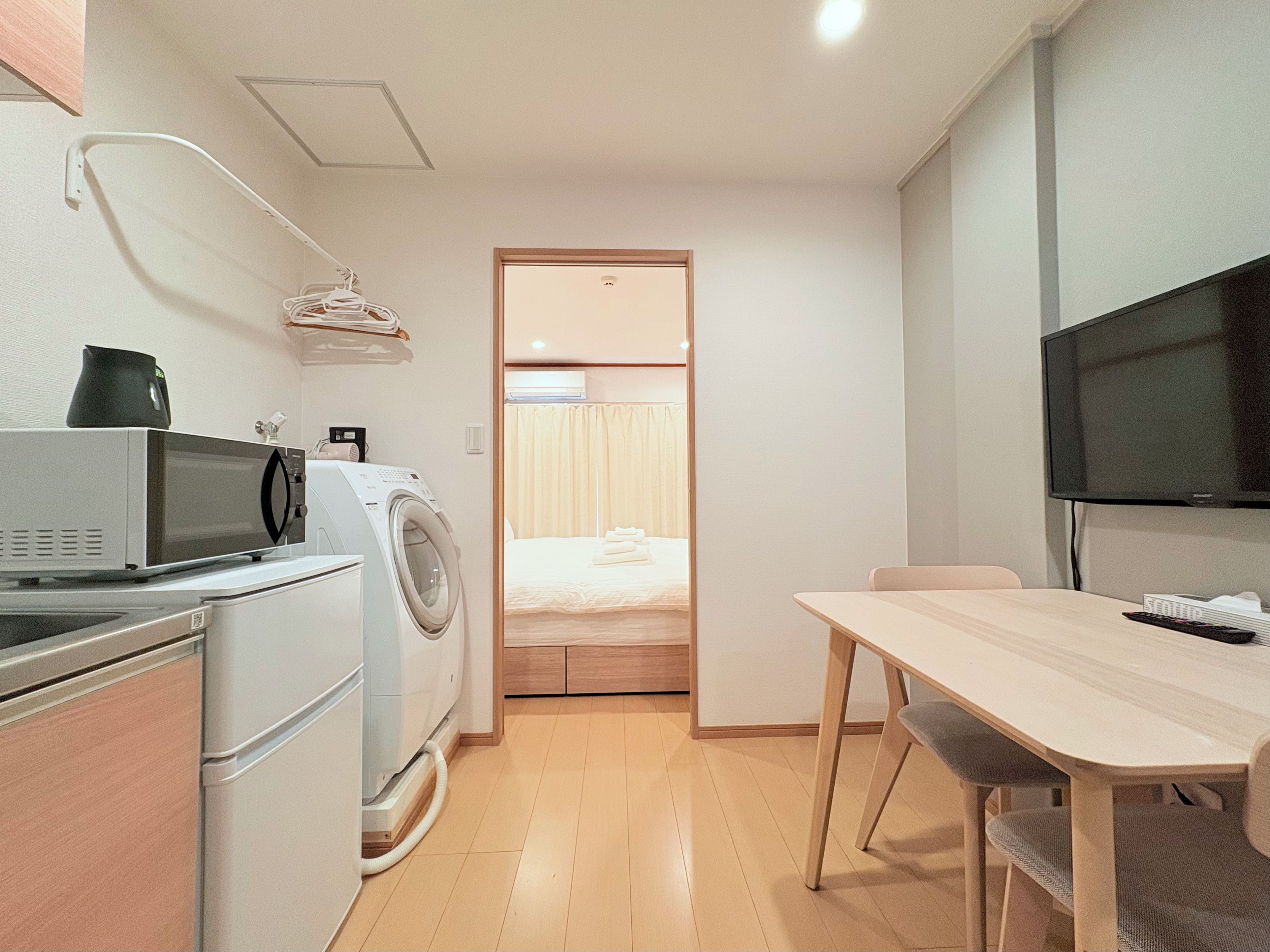 Une chambre d’hôtel compacte comprenant un coin cuisine, un lave-linge, un téléviseur à écran plat, une table à manger avec des chaises et un lit doté de rideaux.