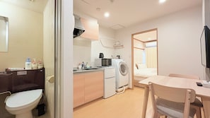 Une chambre d’hôtel compacte comprenant un coin cuisine, un lave-linge, un lit et un petit espace repas.