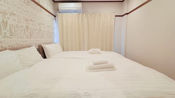 A hotel room with a large bed, a wooden headboard, a wall-mounted air conditioner, and a curtain.