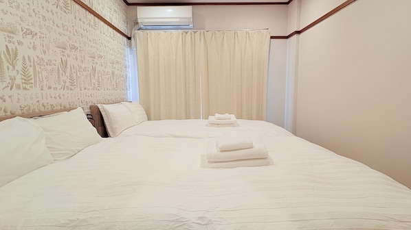 Une chambre d’hôtel avec un grand lit, une tête de lit en bois, un climatiseur fixé au mur et un rideau.