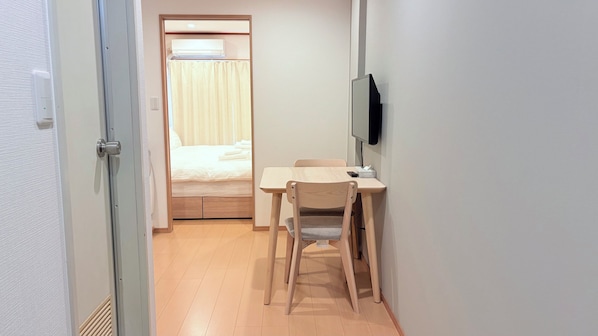 A hotel room with a bed, a desk, a chair, a TV mounted on the wall, and a door leading to another room.