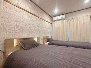 A room with two beds, a patterned wallpaper, an air conditioning unit, and a window with curtains. - Aoba Residence Designer Apartments 302 (大阪市)