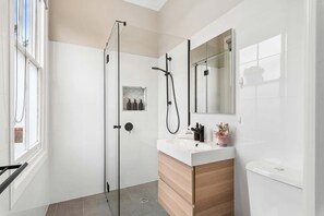 A modern bathroom with a glass shower enclosure, a white vanity with a mirror, and a toilet. - Central Bendigo Charmer, Sleeps 6 (Bendigo)