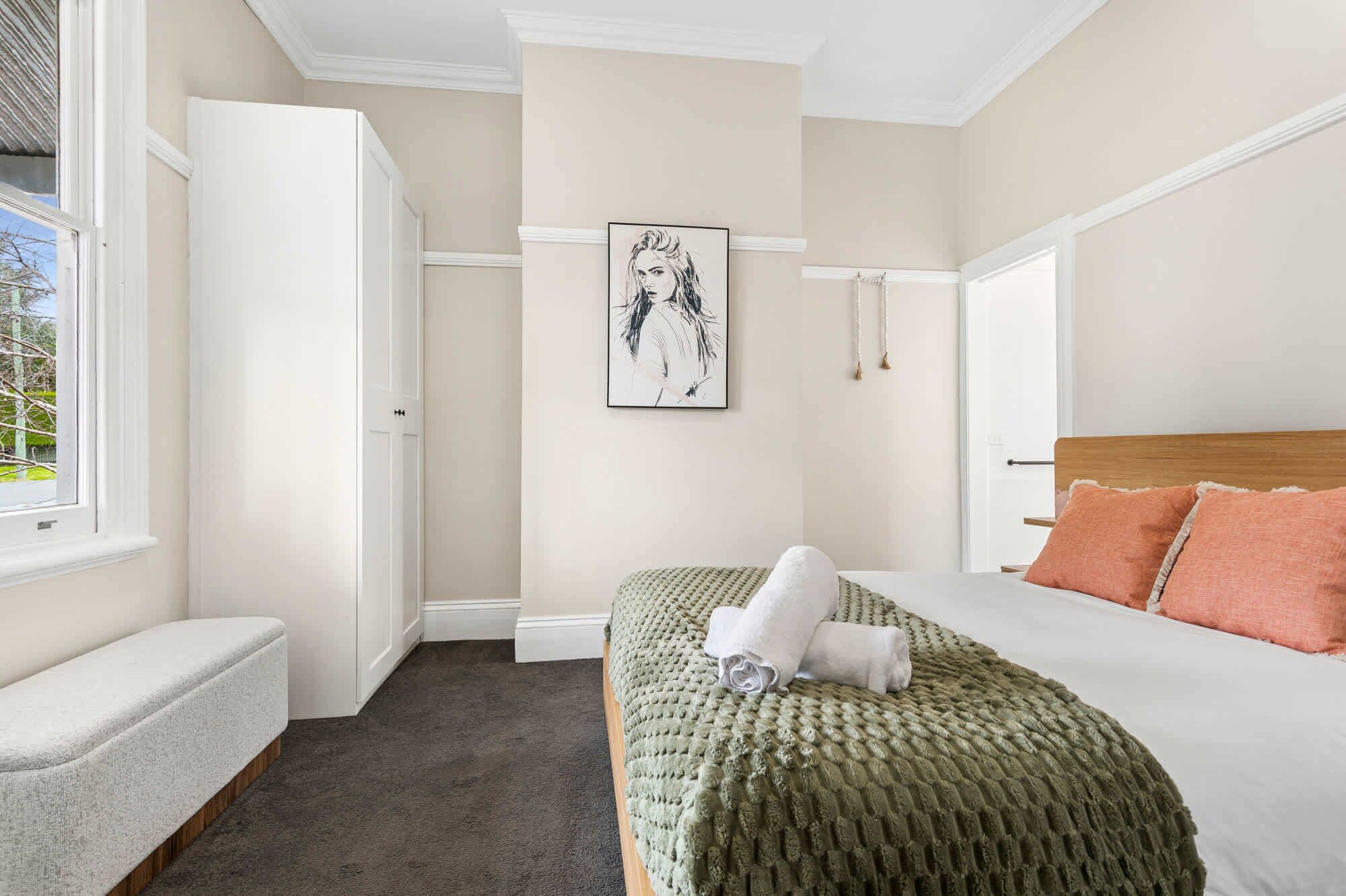 Une chambre à coucher avec un lit, un banc, une porte et une œuvre d’art encadrée accrochée au mur.