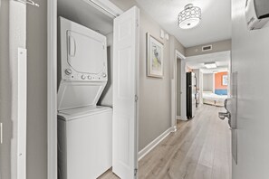A laundry room with a front-loading washer and dryer, a hallway with a door leading to a bedroom, and a ceiling light fixture. - Oceanfront Penthouse, Pool, Lazy River & Waterpark (North Myrtle Beach)