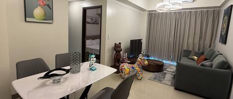 A modern living room with a grey sofa, a dining table with chairs, and a TV.