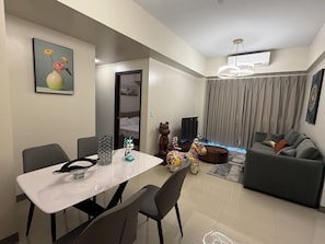 Una sala de estar moderna con un sofá gris, una mesa de comedor con sillas y un televisor.