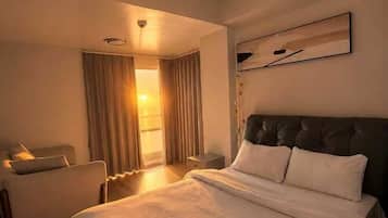 A hotel room with a large bed, a seating area, and a view of the outdoors.