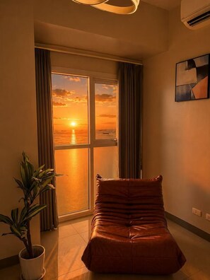 Una habitación con un ventanal grande, un sofá de cuero marrón, una planta en maceta y un cuadro en la pared.