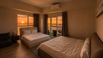 A hotel room with two beds, a nightstand, a chair, and a view of a sunset over a body of water.