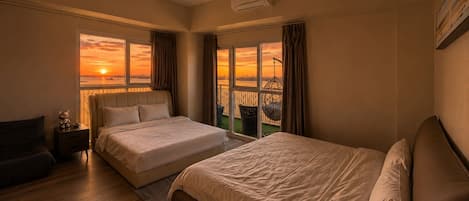 A hotel room with two beds, a nightstand, a chair, and a view of a sunset over a body of water.