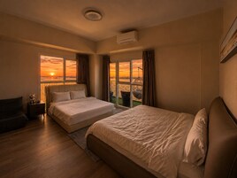 Habitación de hotel con dos camas, una mesita de noche, una silla y vista a un atardecer sobre el agua.