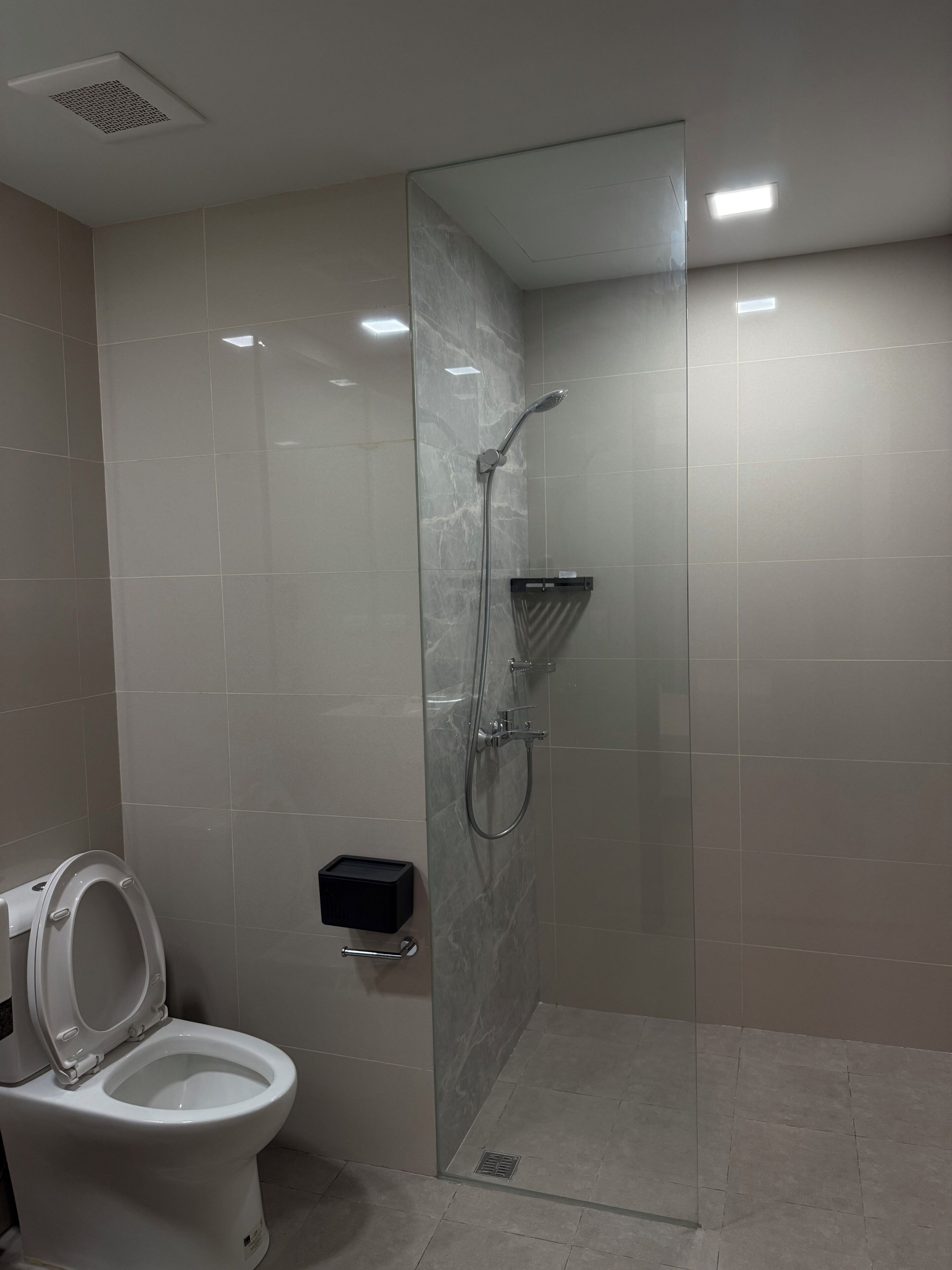 A modern bathroom with a glass-enclosed shower, a toilet, and a soap dispenser.