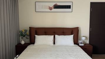 Una camera d'albergo con un letto grande, una testiera, un comodino con una lampada, un quadro incorniciato al muro e una finestra con tende.