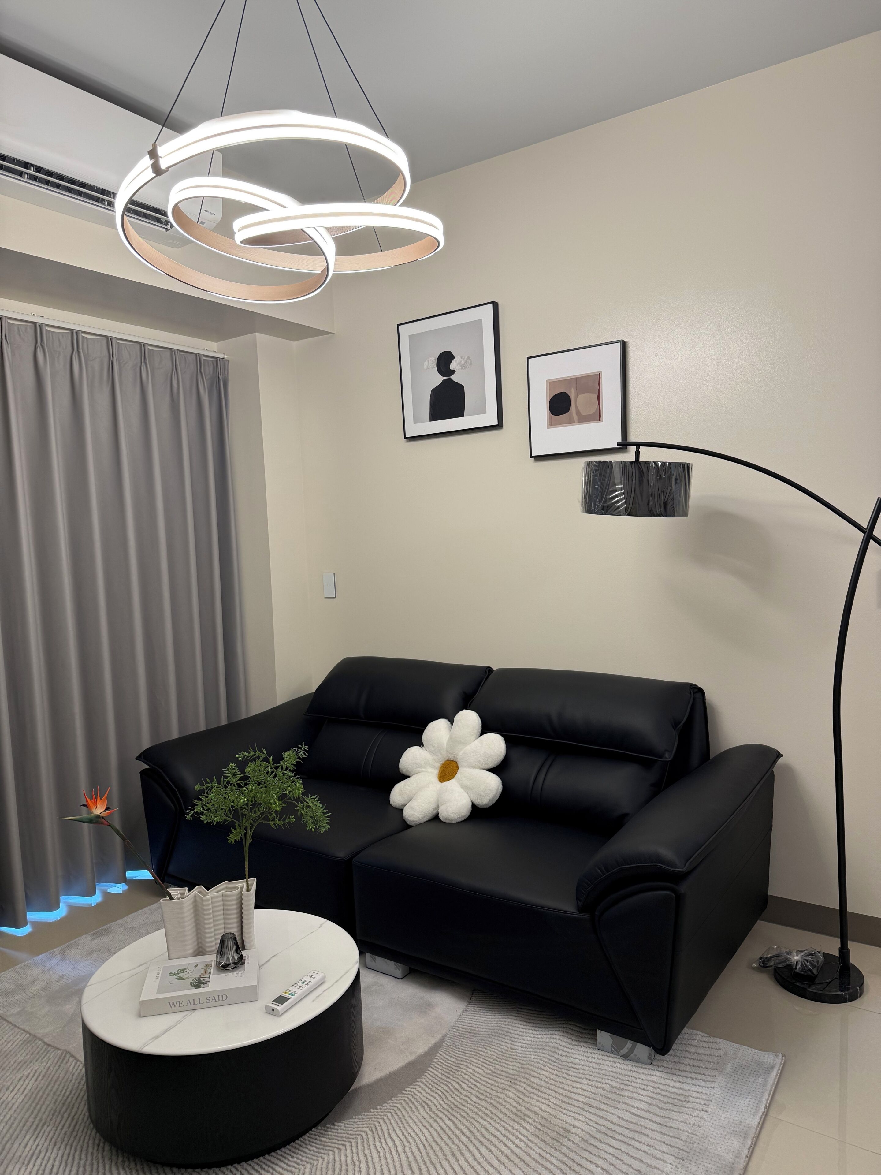 A modern living room with a black leather sofa, a round coffee table, and a unique white flower-shaped pillow.