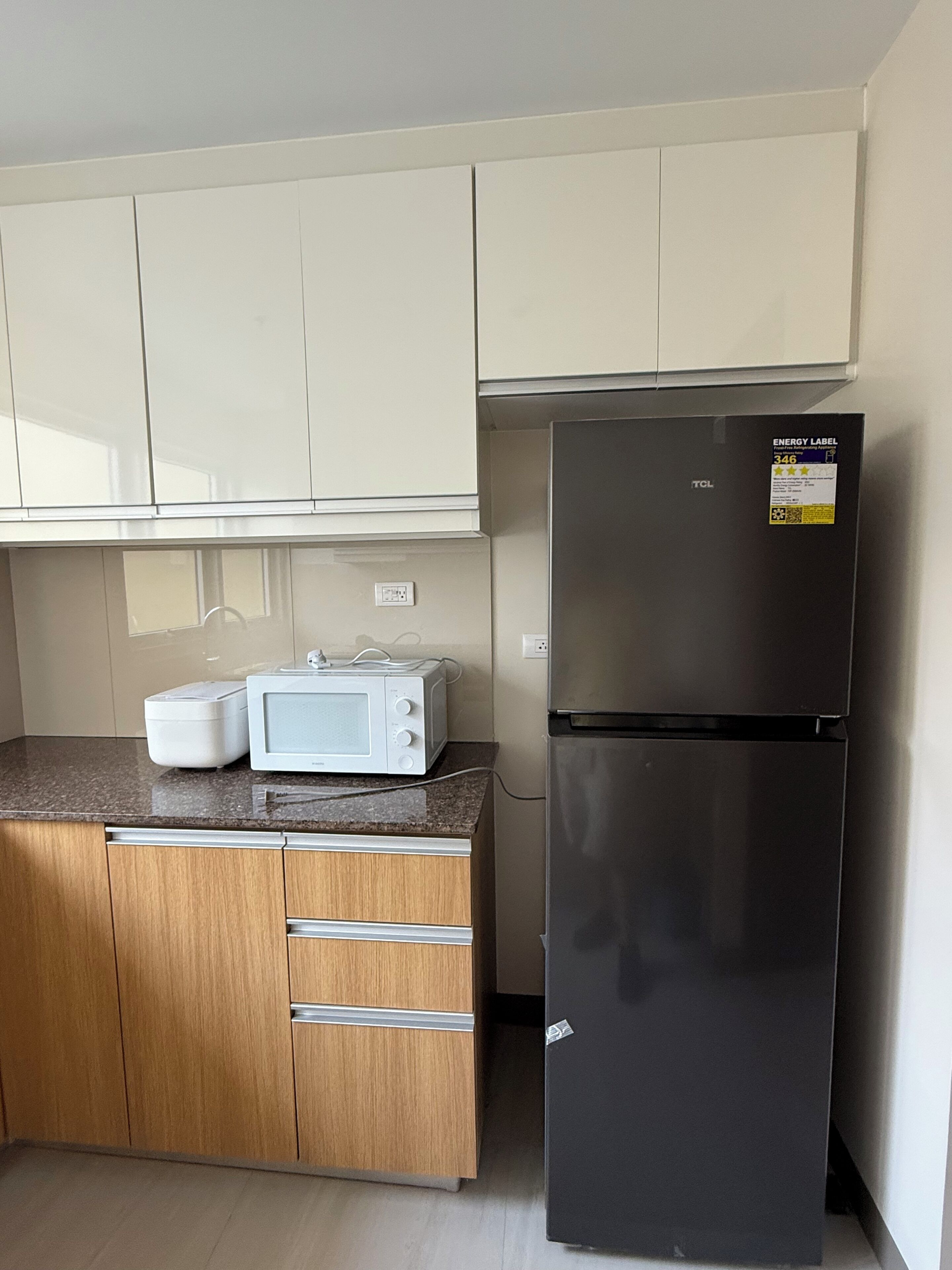 Eine Küche mit einer Mikrowelle, einem schwarzen Kühlschrank, Holzschränken und einer Arbeitsplatte.
