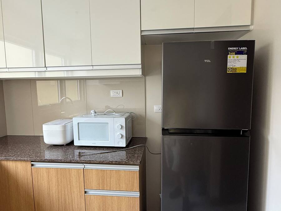 Een keuken met een magnetron, een zwarte koelkast, houten kastjes en een aanrecht.