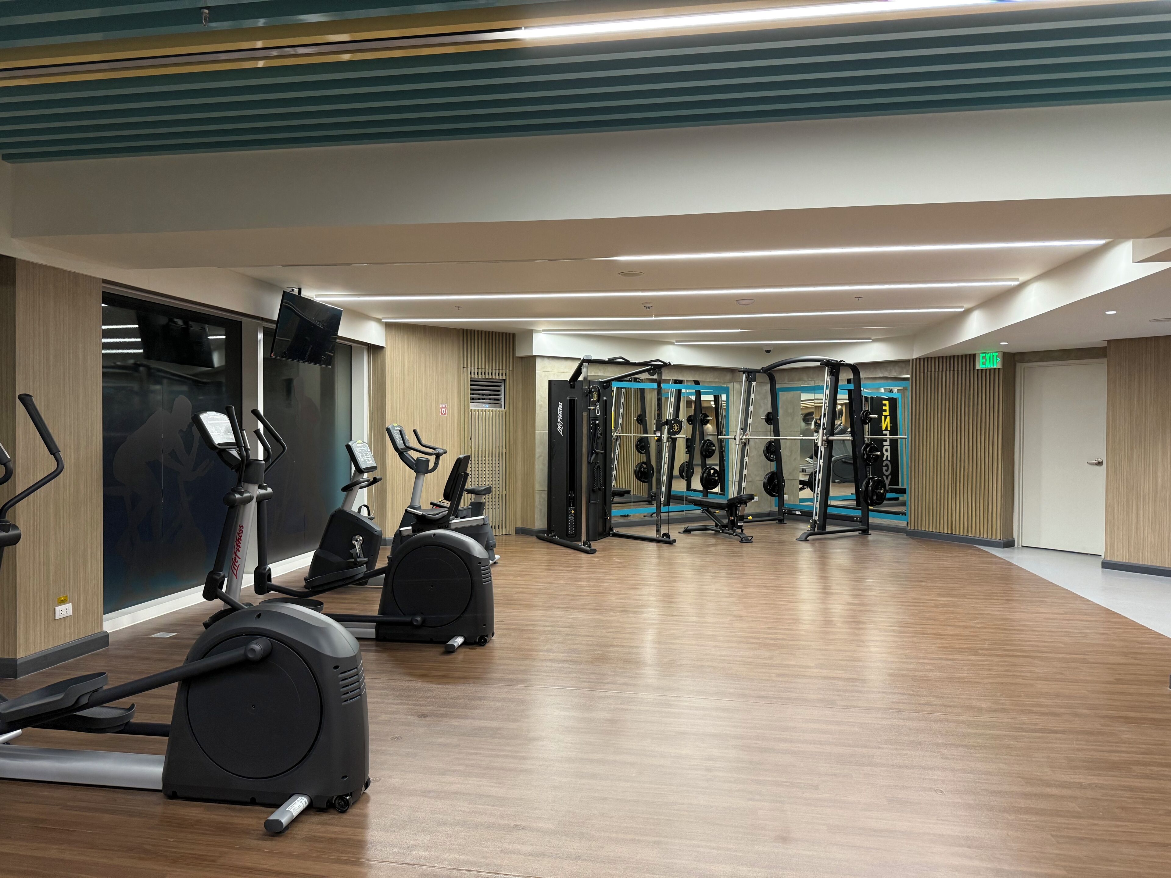 A gym with cardio machines, weightlifting equipment, and a mirror on the wall.