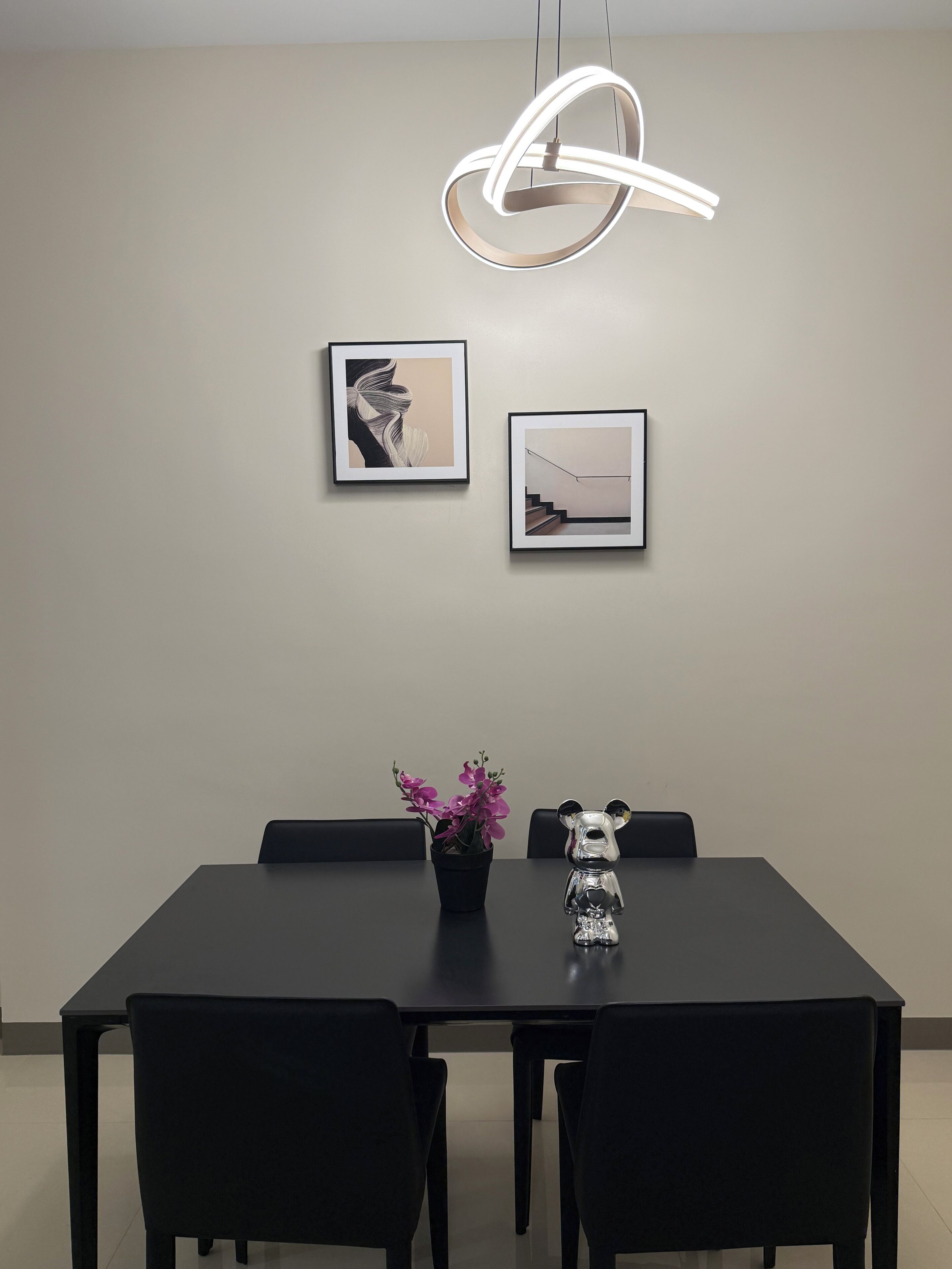 A modern dining area with a black table, four chairs, a potted plant with purple flowers, and two framed pictures on the wall.