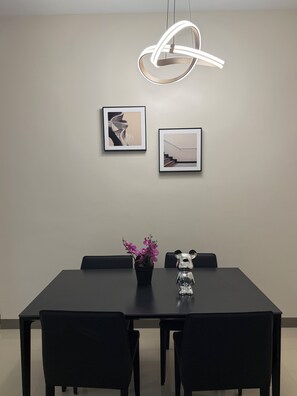 A modern dining area with a black table, four chairs, a potted plant with purple flowers, and two framed pictures on the wall.
