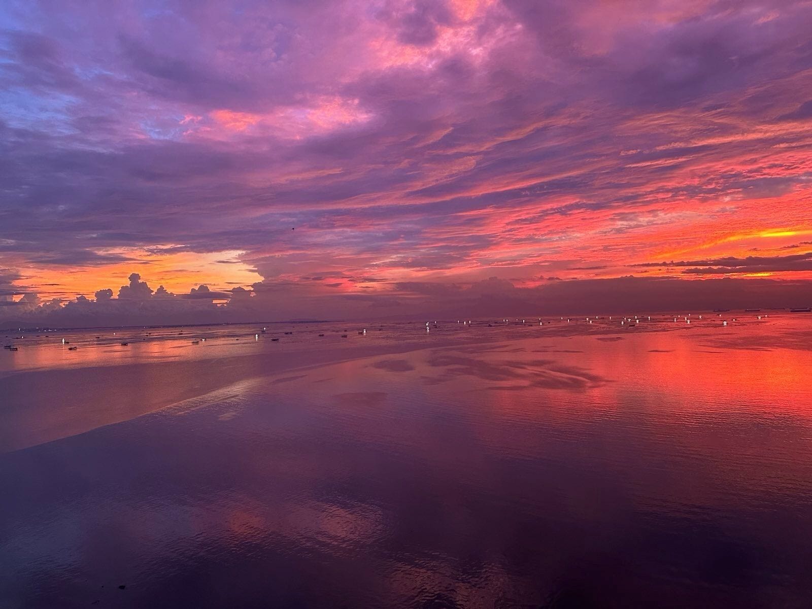 A sunset over a calm body of water with boats and a distant shoreline.