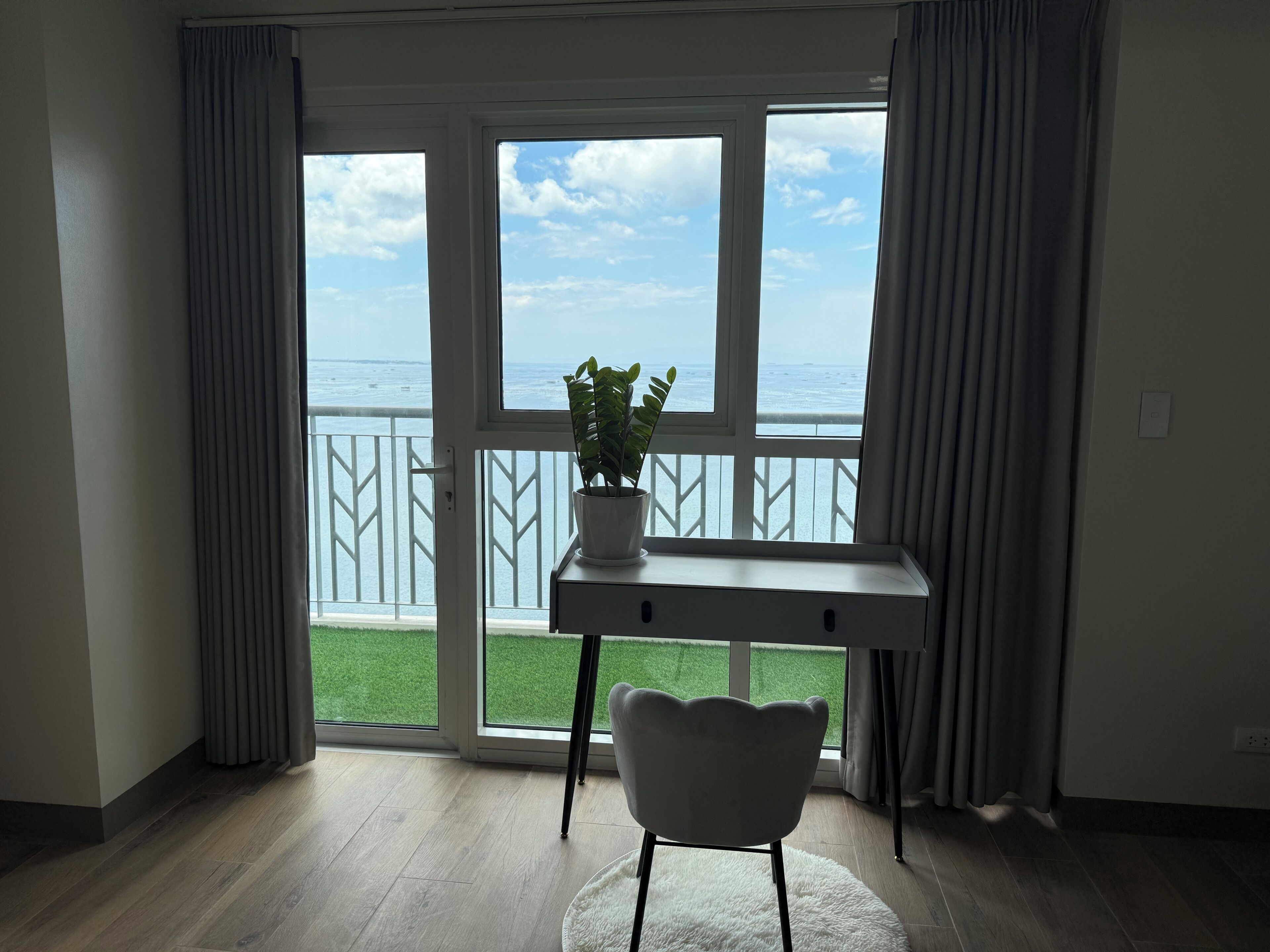 A room with a view of the sea, a desk, a chair, and a potted plant.