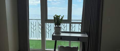 A room with a view of the sea, a desk, a chair, and a potted plant.