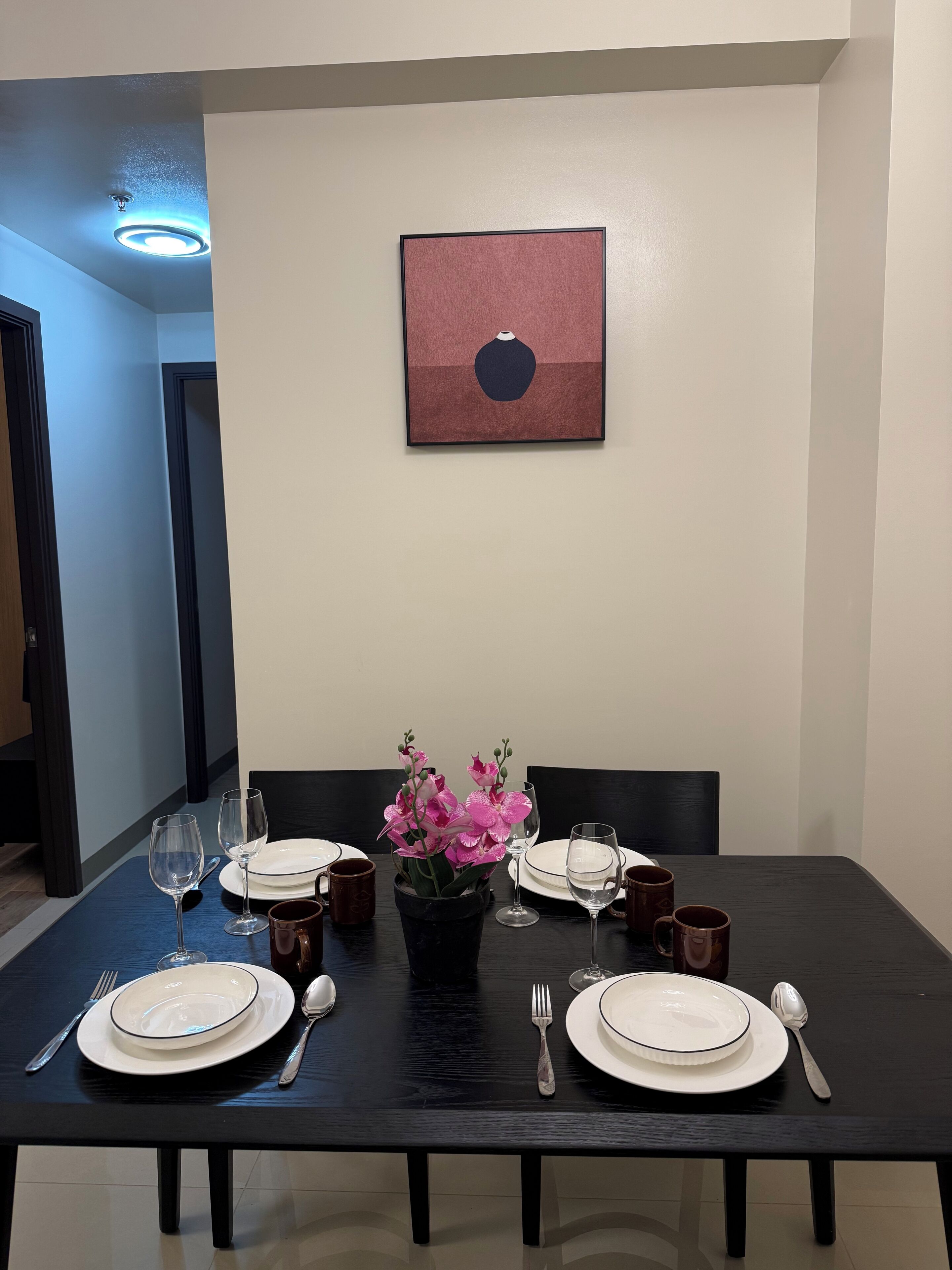 A dining table set with plates, glasses, and cutlery, a vase with flowers, and a framed picture on the wall.