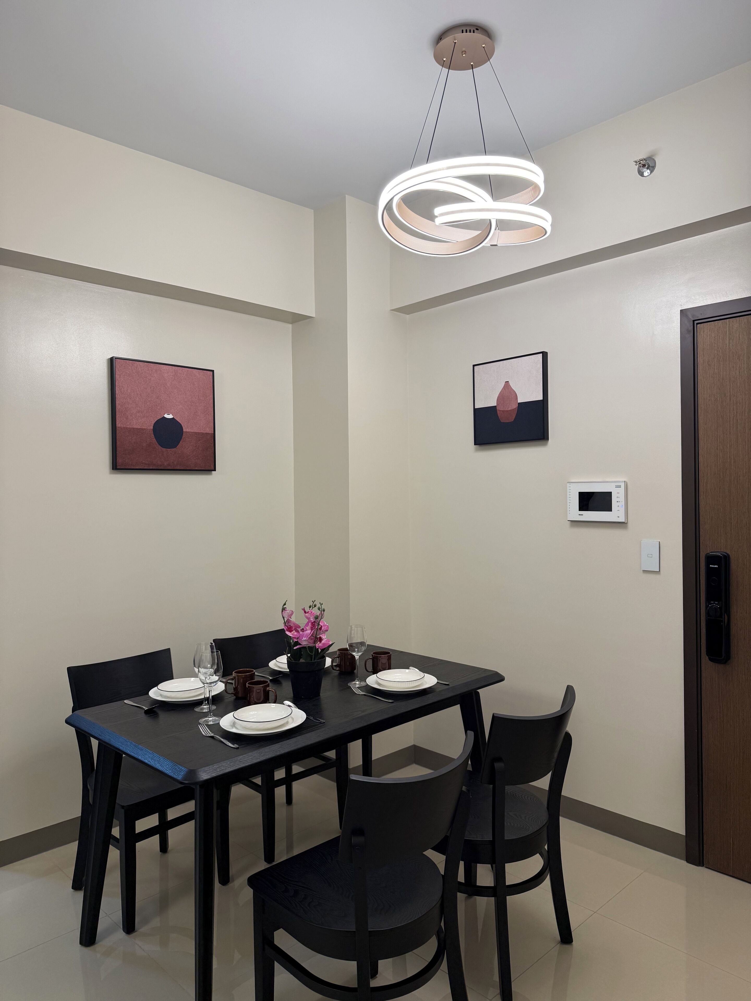 A dining area with a table set for four, chairs, a modern pendant light, and two framed artworks on the walls.