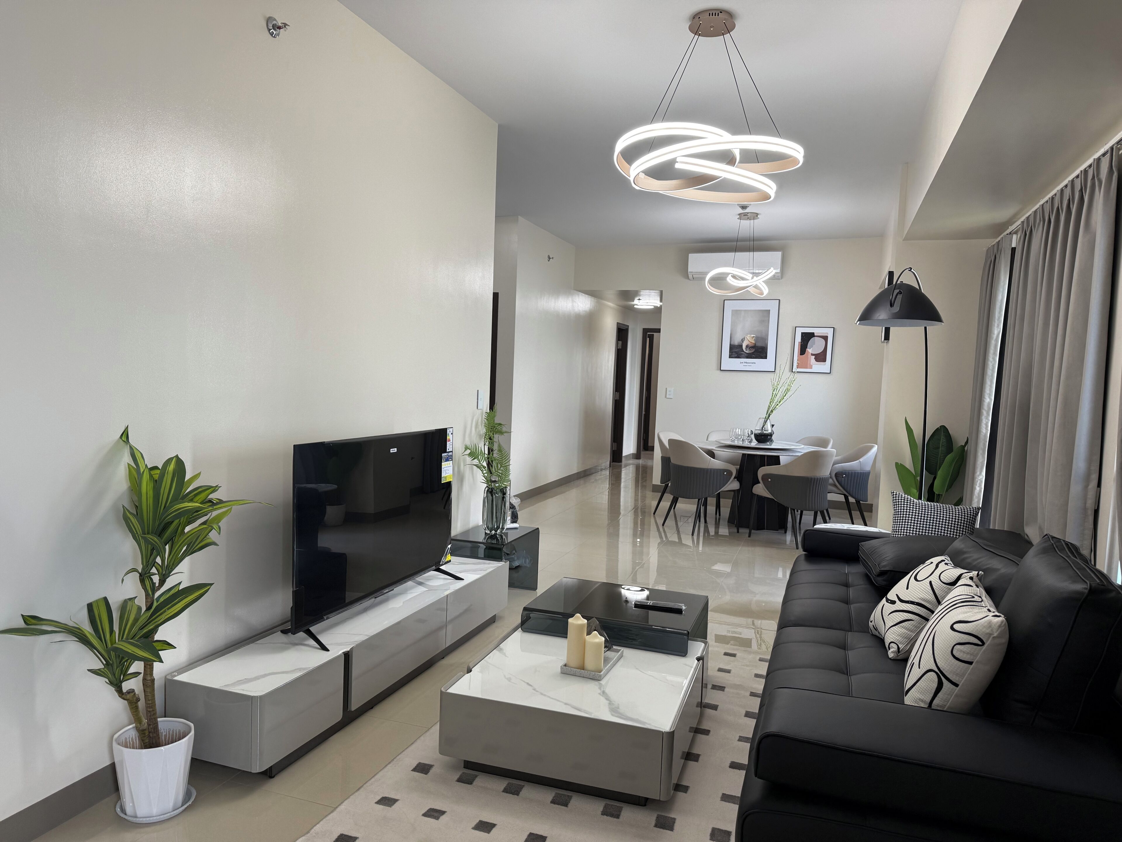 A modern living room with a flat-screen TV, a coffee table, a sofa, and a dining area with chairs.