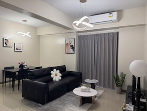 A modern living room with a black sofa, a round coffee table, and a dining area with a table and chairs.