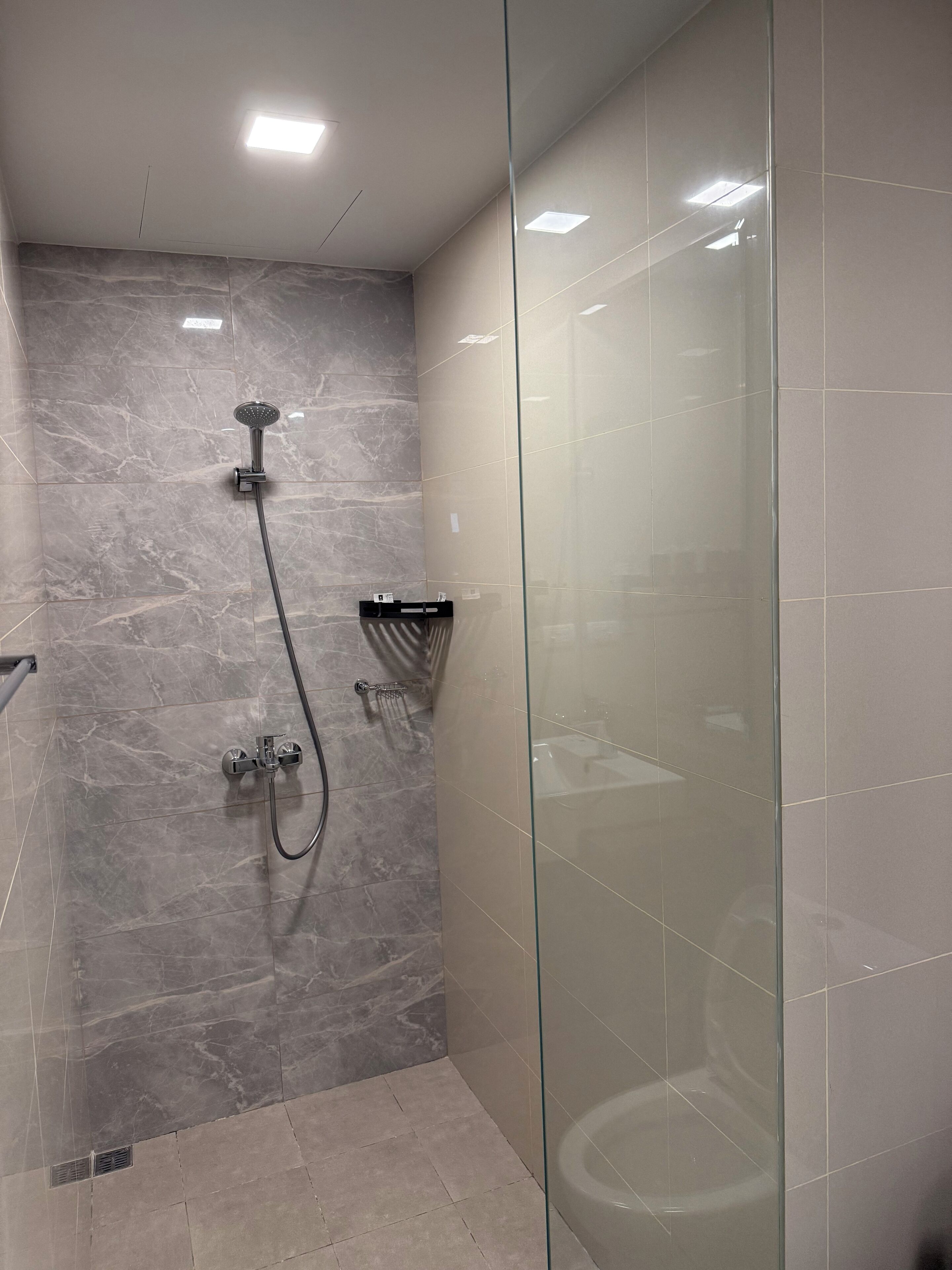 A modern bathroom with a glass shower enclosure, marble walls, and a glass partition.