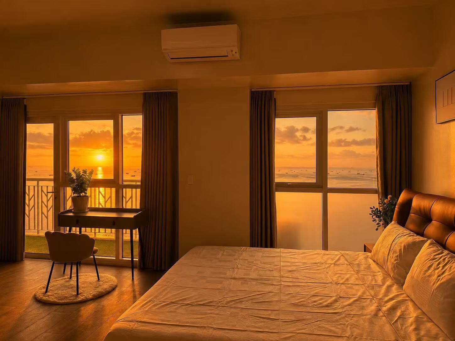 A hotel room with a bed, a desk, and a view of the sunset over the sea.