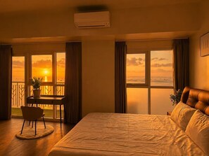 Una habitación de hotel con una cama, un escritorio y vistas a la puesta de sol sobre el mar.