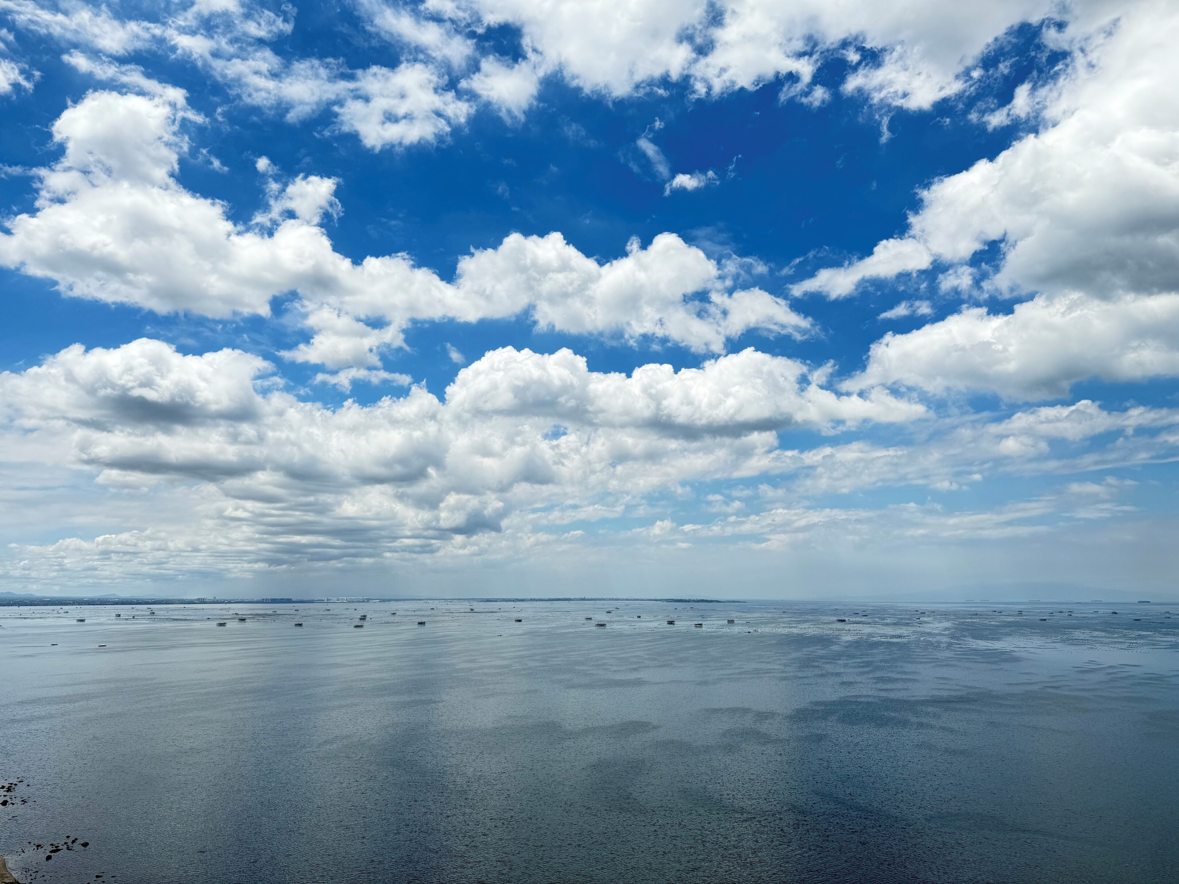 A wide view of a calm sea with scattered boats under a partly cloudy sky.