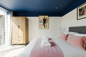 A hotel room with a bed, a wardrobe, a poster, a fan, and a window. - GuestReady - Gated West London Retreat (NO WIFI) (London)