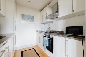 A modern kitchen with white cabinets, a stainless steel range, an oven, a microwave, and a window with a view. - GuestReady - Gated West London Retreat (NO WIFI) (London)
