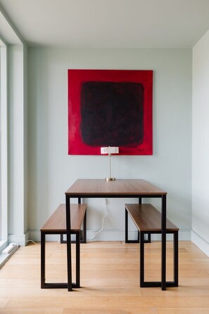 Una habitación con piso de madera, una mesa con un banco y un cuadro abstracto rojo en la pared.
