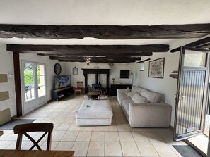 Uma sala de estar com sofá, banqueta e lareira. Há uma televisão e um espaço de jantar com mesa e cadeiras.